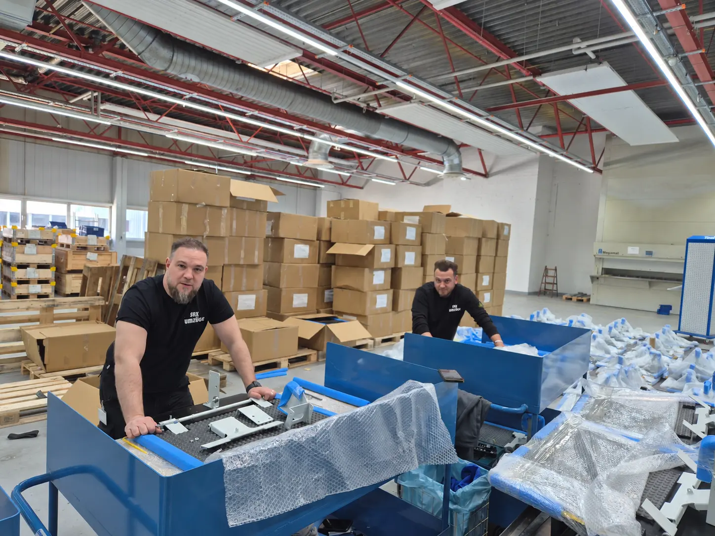 Zwei SAX-Kollegen bei der Arbeit zwischen Transportwagen, Schutzmaterial und Kartons.